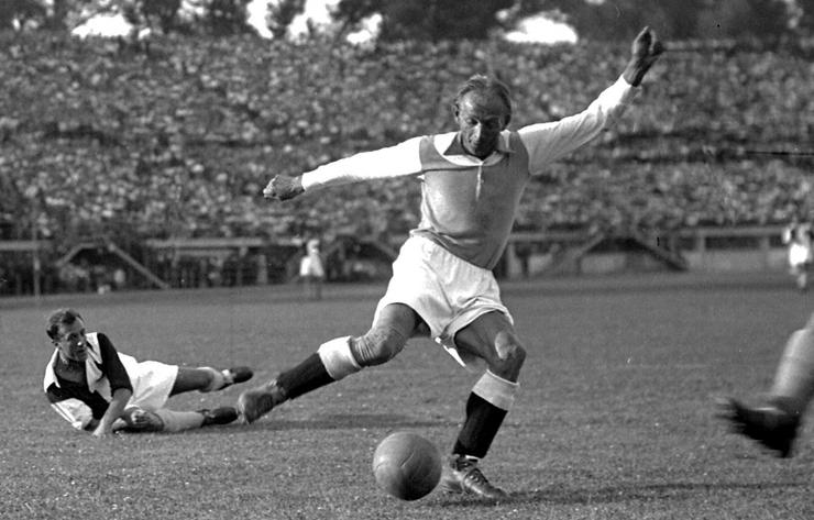 Matthias Sindelar kicking the ball as a helpless player looks on in the background.